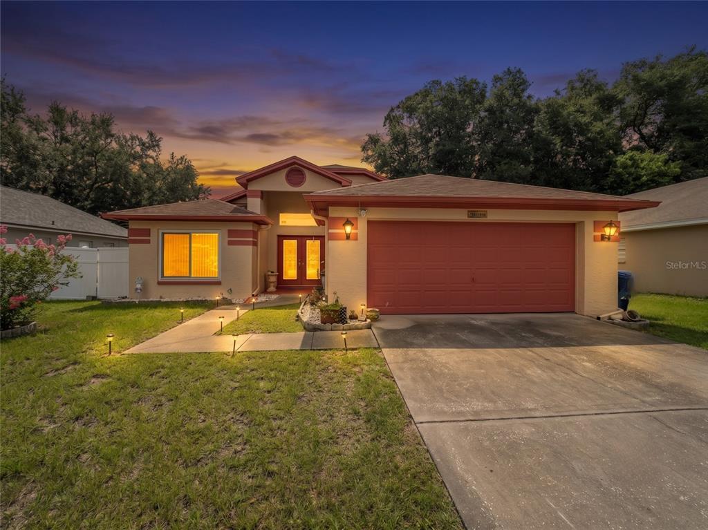A single-story house with a red garage door, tan stucco exterior, and a concrete driveway — 1604 COPPERSMITH COURT, LUTZ, FL