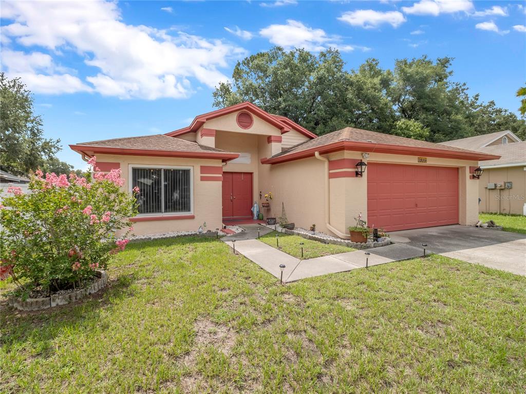 A single-story house with tan stucco walls, red trim, and a two-car garage — 1604 COPPERSMITH COURT, LUTZ, FL