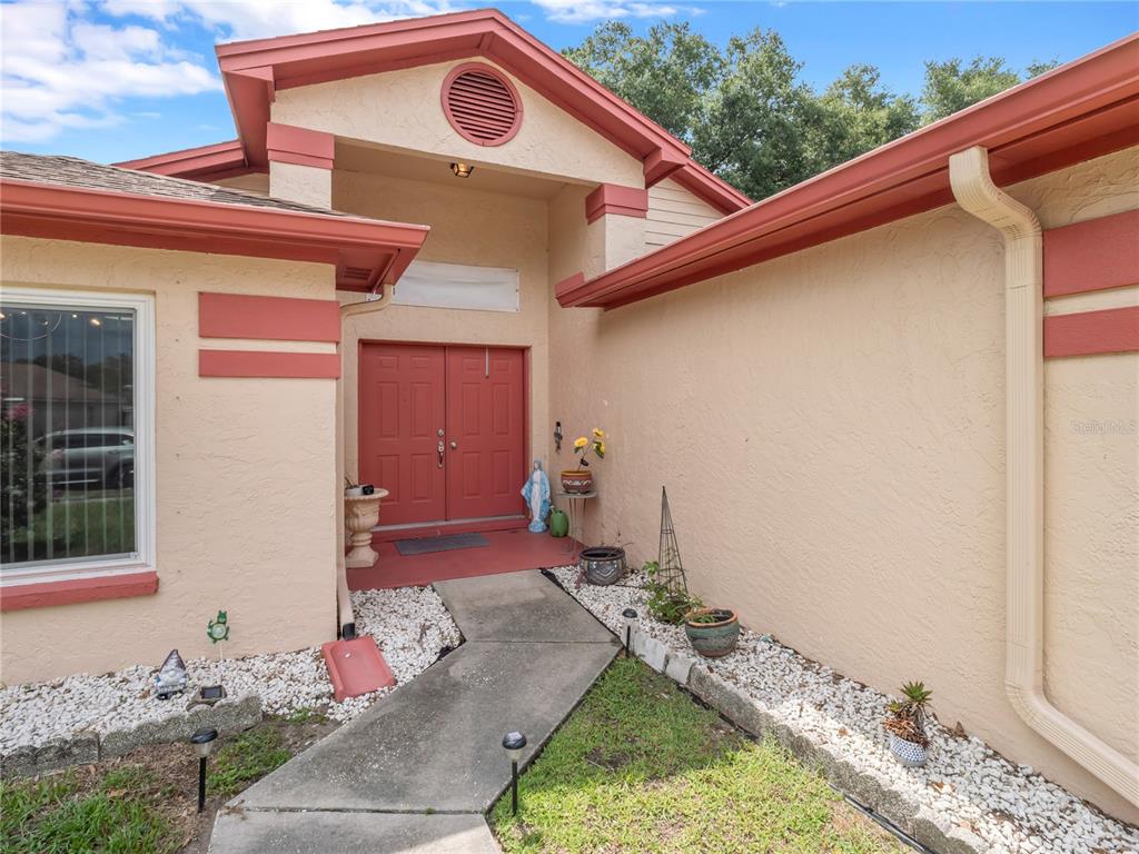 The exterior of a house features a tan stucco facade, red trim, and a double-door entrance — 1604 COPPERSMITH COURT, LUTZ, FL