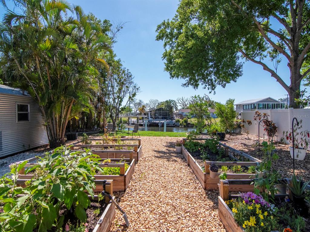 A backyard garden features raised wooden planter beds, gravel paths, and a view of water — 106 STEVEN STREET, RUSKIN, FL