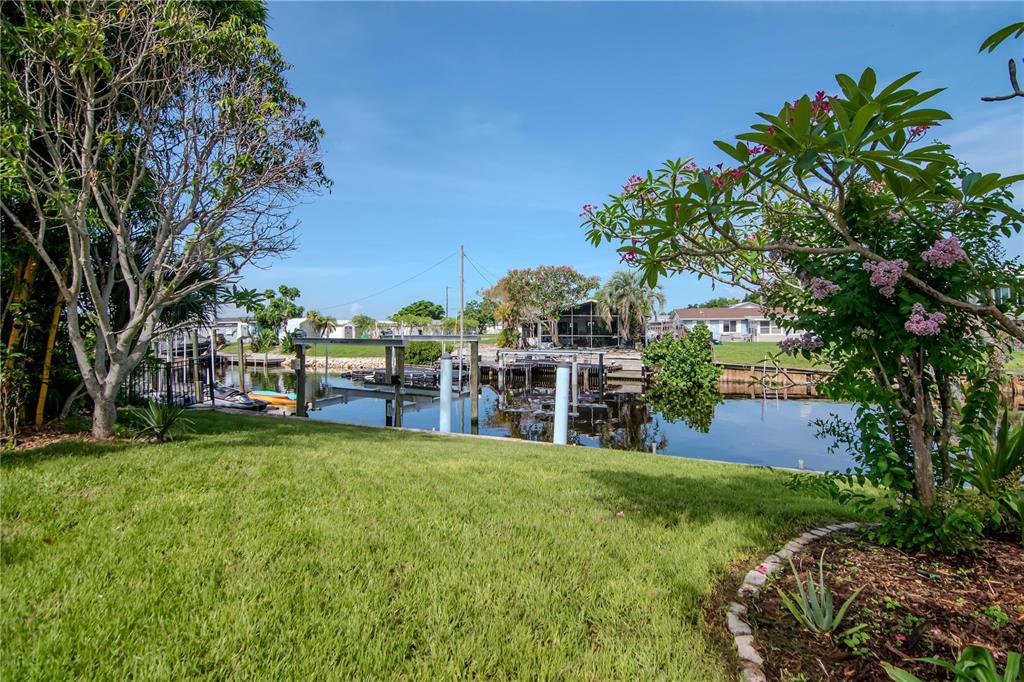 A grassy backyard overlooks a canal with a private boat dock and surrounding tropical landscaping — 106 STEVEN STREET, RUSKIN, FL
