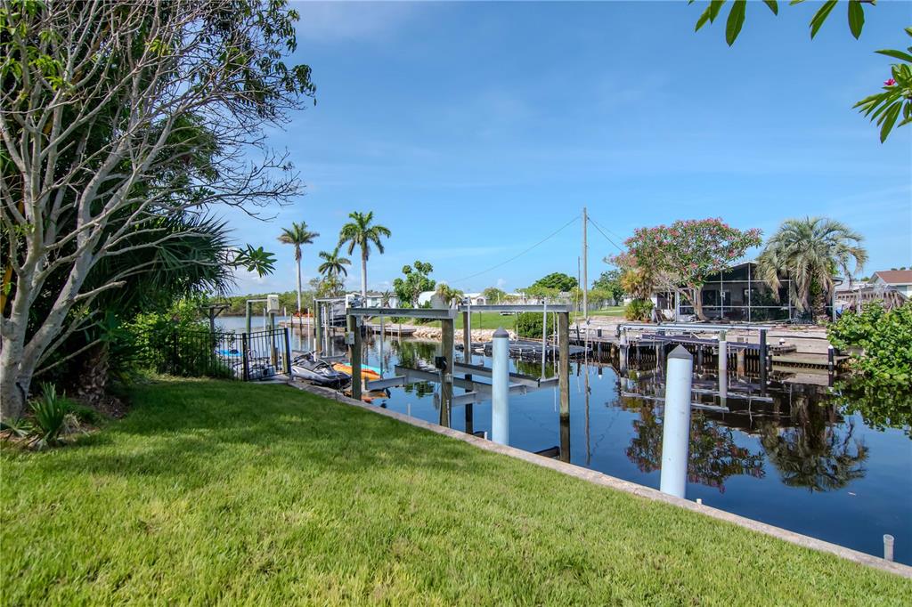 A grassy backyard leads to a private canal with a boat lift and dock — 106 STEVEN STREET, RUSKIN, FL