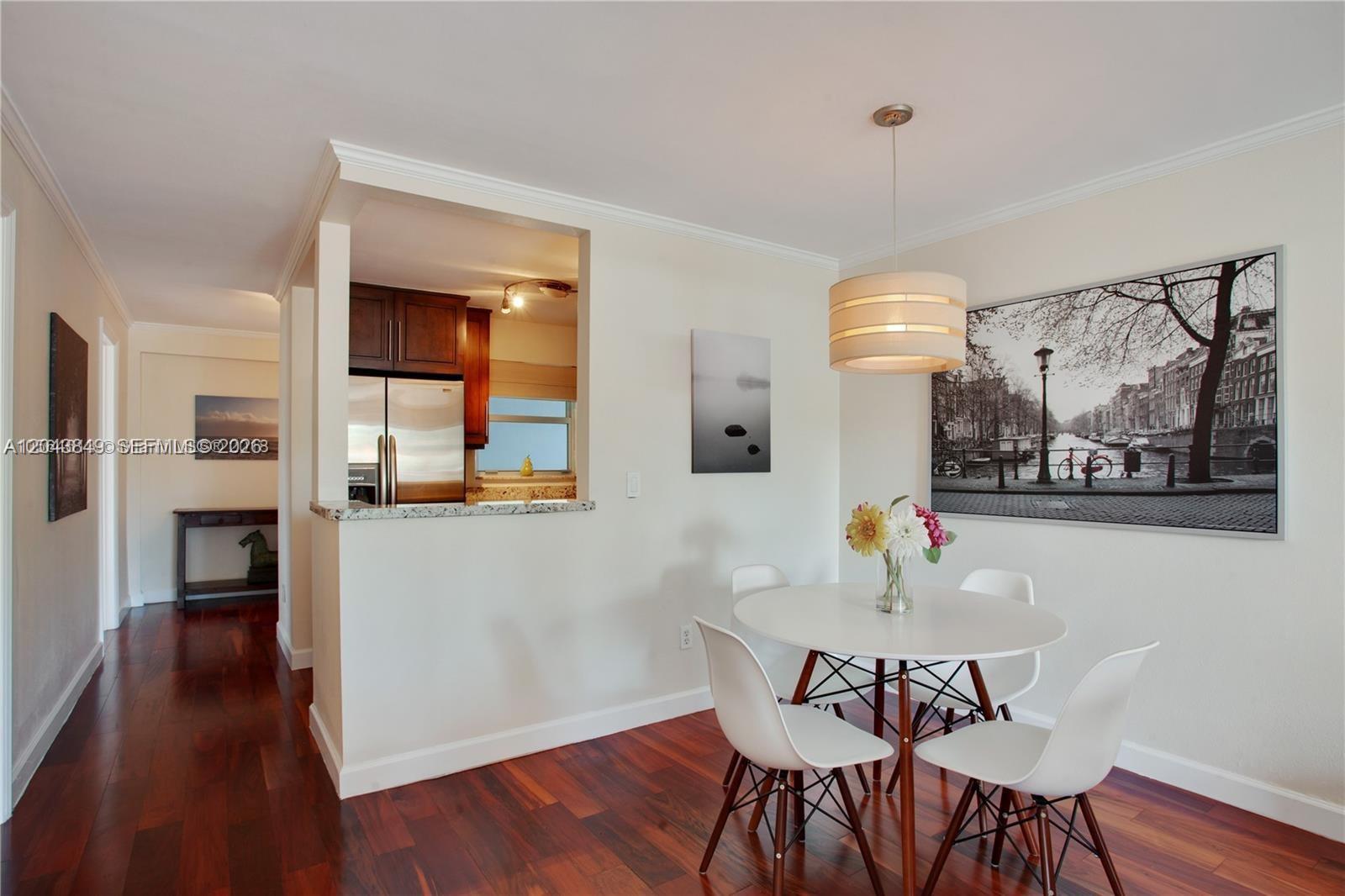 A dining area with a round white table and chairs sits next to a kitchen pass-through — 1610 Lenox Ave # 301, Miami Beach FL 33139, MIAMI BEACH, FL