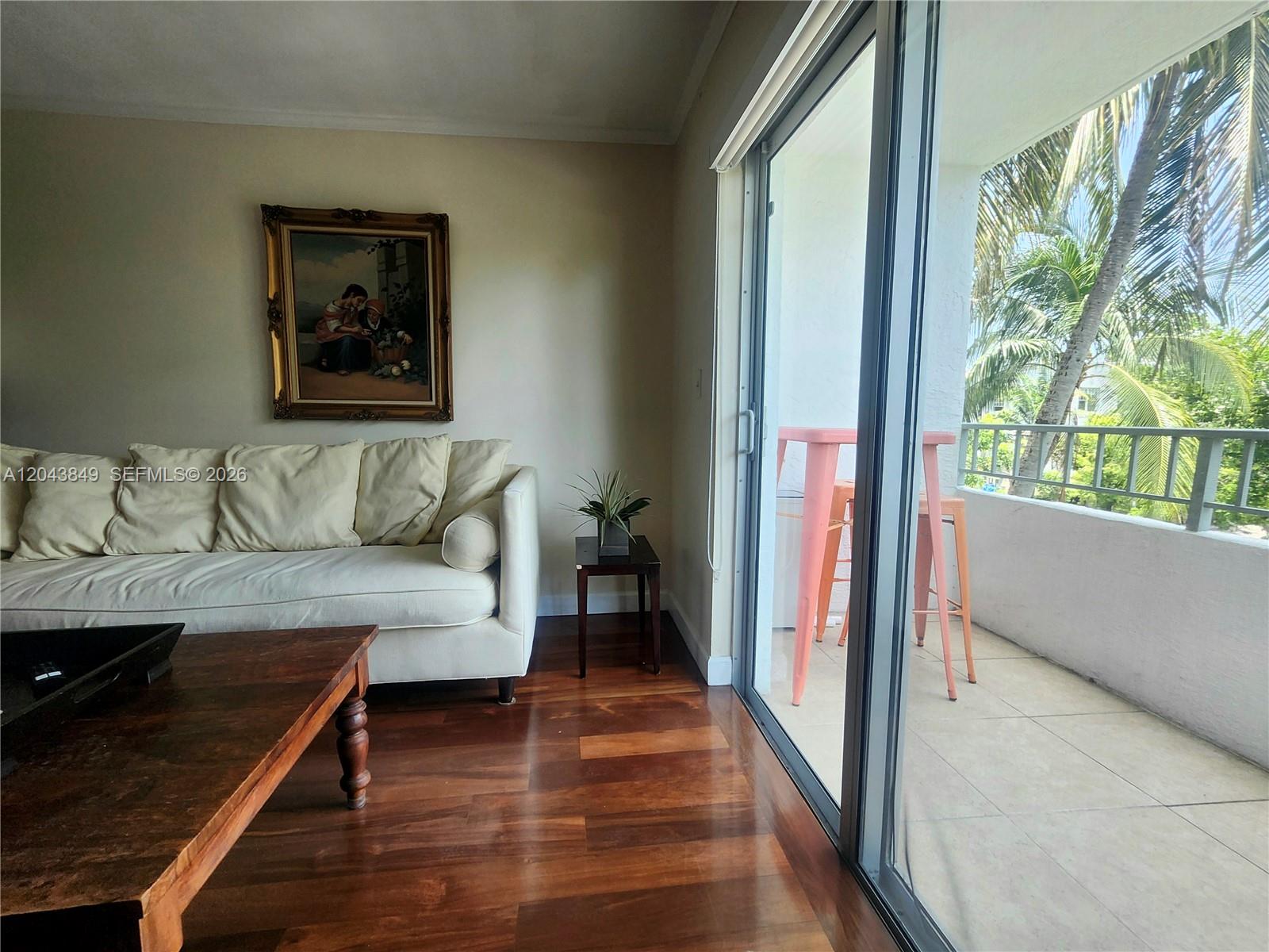A living room with hardwood floors, a white sofa, and a balcony with palm trees — 1610 Lenox Ave # 301, Miami Beach FL 33139, MIAMI BEACH, FL