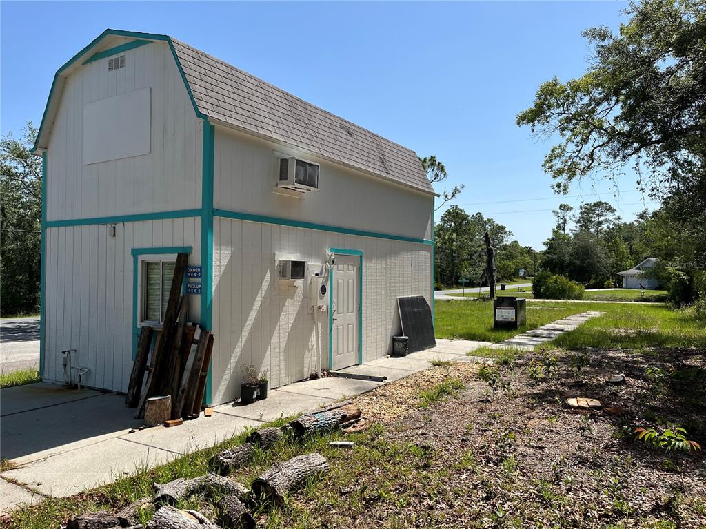 A two-story white barn-style building with turquoise trim sits on a concrete lot — 18132 COMMERCIAL WAY, WEEKI WACHEE, FL