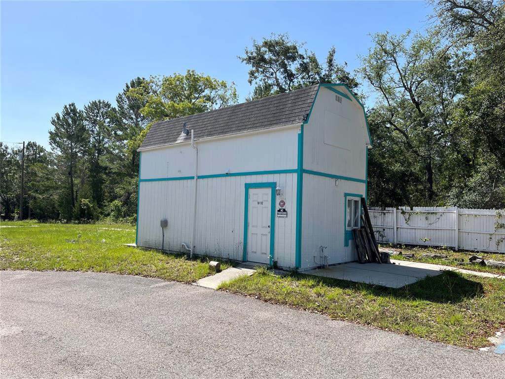 A white, two-story barn-style shed with teal trim sits on a concrete pad outdoors — 18132 COMMERCIAL WAY, WEEKI WACHEE, FL