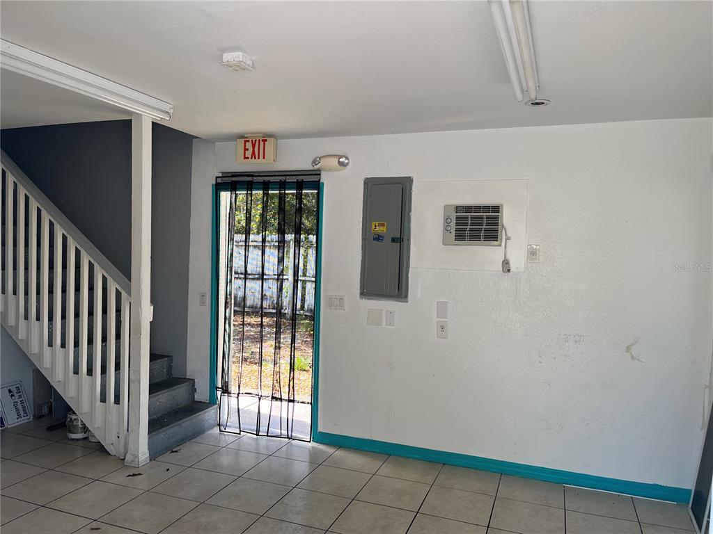 A room with tile flooring, a staircase, an exit door, and a wall-mounted air conditioner — 18132 COMMERCIAL WAY, WEEKI WACHEE, FL