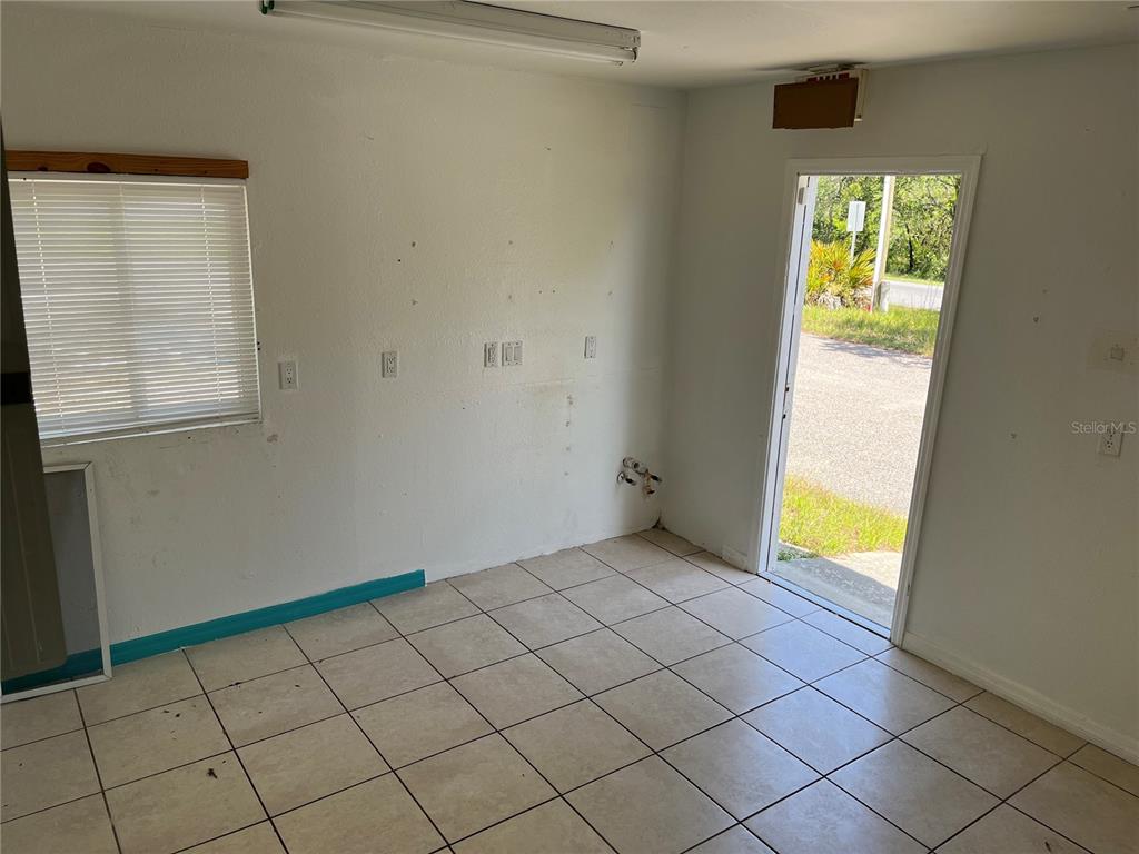 A room with white walls, tiled flooring, a window with blinds, and an open exterior door — 18132 COMMERCIAL WAY, WEEKI WACHEE, FL
