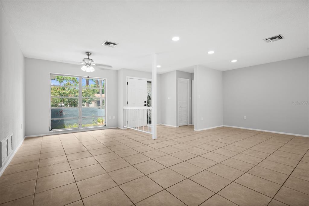 An empty living room features light-colored tile flooring, a ceiling fan, and a white railing — 504 BAMBOO COURT, TARPON SPRINGS, FL