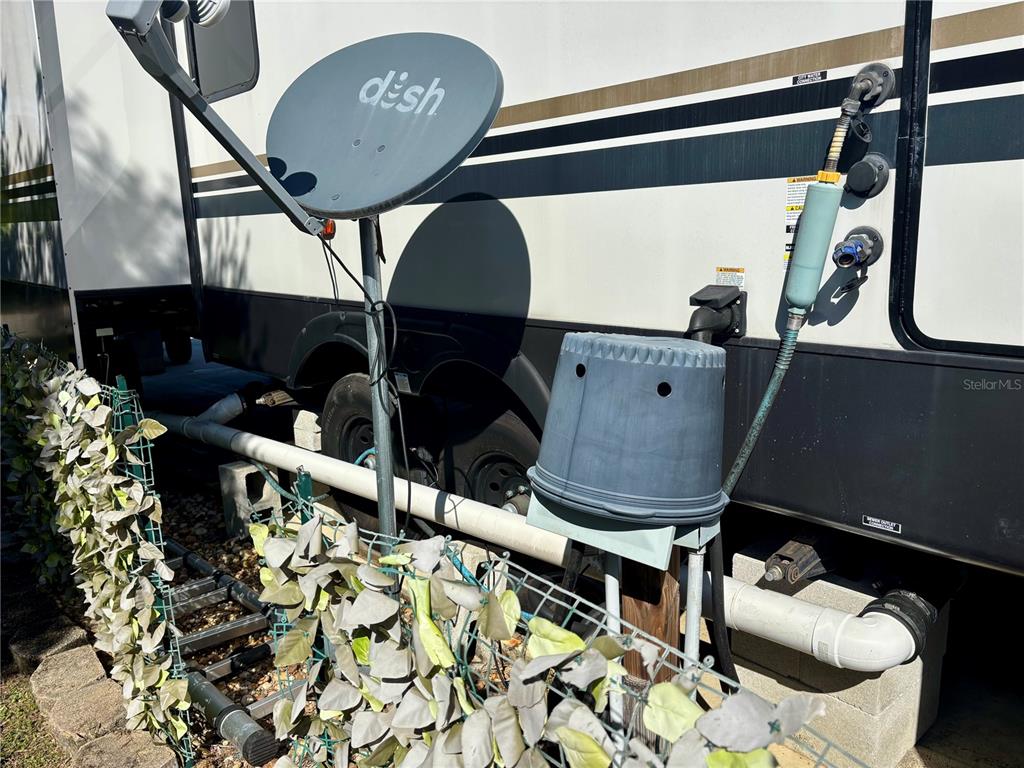 An exterior view of a recreational vehicle featuring a satellite dish and plumbing connections — 3259 NE 102ND AVENUE ROAD, SILVER SPRINGS, FL