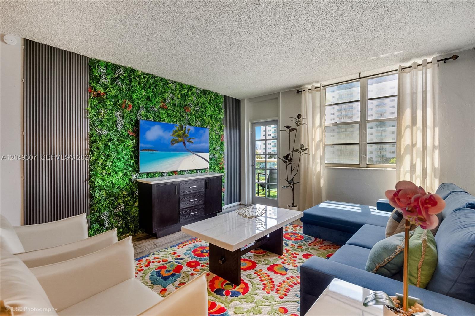 A living room features a green wall accent, a television, and a colorful patterned rug — SUNNY ISLES BEACH, FL
