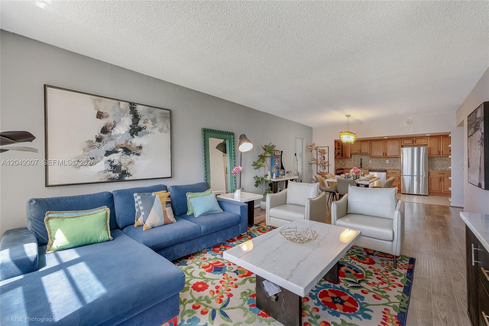 A living room features a blue sectional sofa, two white armchairs, and a floral rug — SUNNY ISLES BEACH, FL
