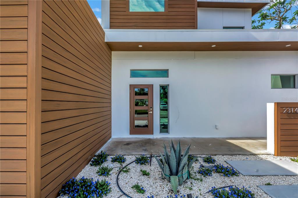 The exterior of a modern home features wood-slat siding, a brown front door, and landscaping — 2314 FLOYD STREET, SARASOTA, FL