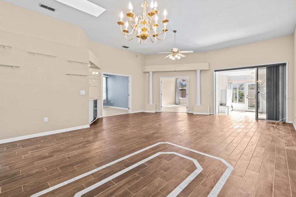 A spacious living room features wood-look tile flooring, a crystal chandelier, and a sliding glass door — 2788 COUNTRY WAY, CLEARWATER, FL