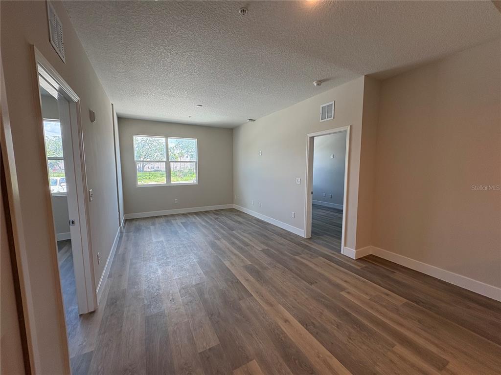 An empty room features wood-look flooring, light-colored walls, and a window overlooking an outdoor area — 4424 S TEXAS AVENUE UNIT 1-104, ORLANDO, FL