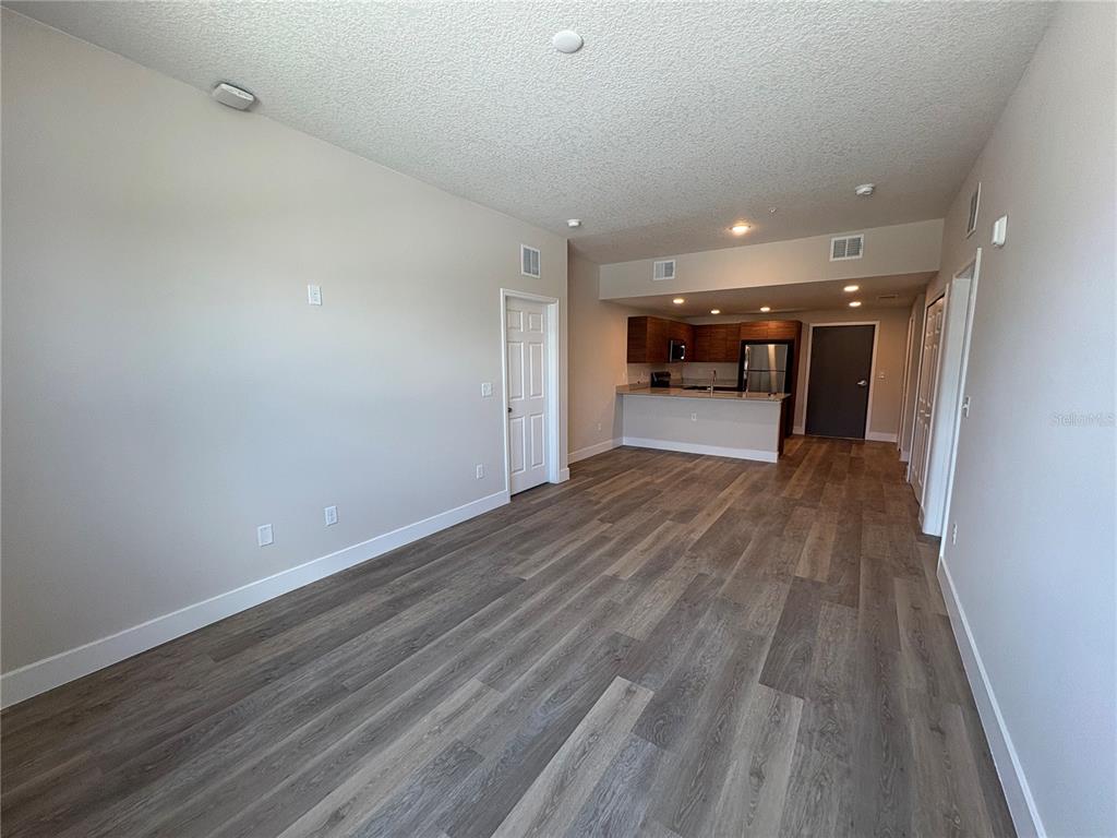 An open-concept living area features wood-look flooring, neutral walls, and an adjacent kitchen with cabinets — 4424 S TEXAS AVENUE UNIT 1-104, ORLANDO, FL