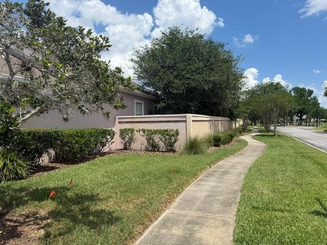 A sidewalk runs alongside a pink exterior wall, a hedge, and trees under a blue sky — 14453 WINDCHIME LANE, ORLANDO, FL
