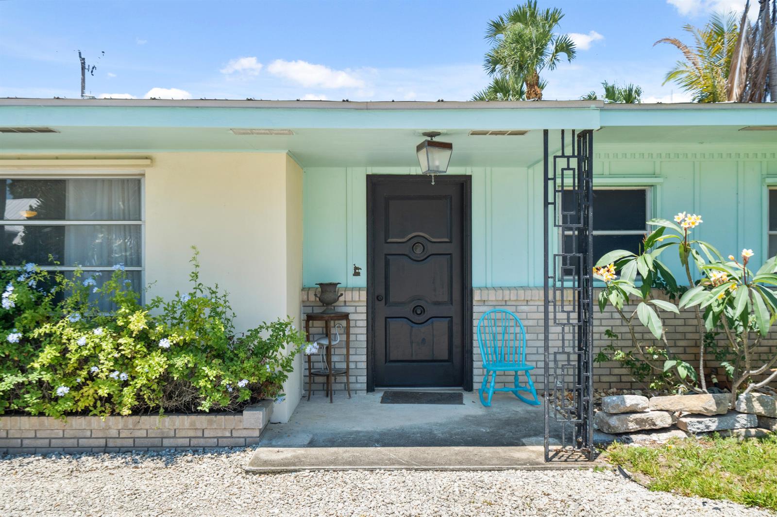 A light-colored house exterior features a dark front door, a turquoise rocking chair, and landscaping — 1644 NE Arch Avenue, Jensen Beach FL 34957, JENSEN BEACH, FL