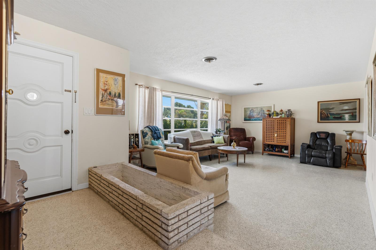 A living room features a brick planter, beige carpeting, and a white front door — 1644 NE Arch Avenue, Jensen Beach FL 34957, JENSEN BEACH, FL