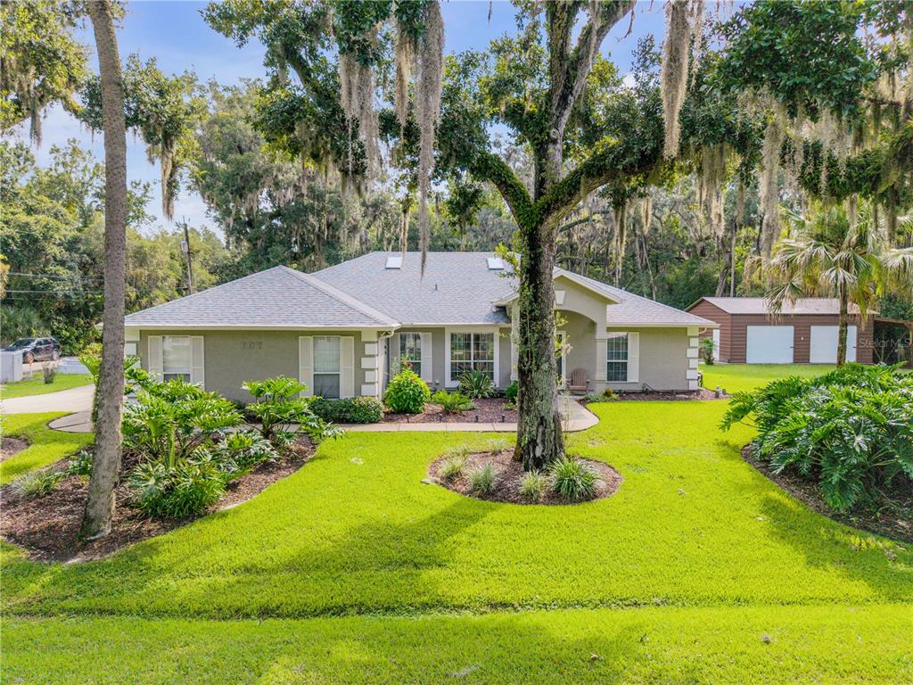 A single-story house with a grey roof, light-colored siding, and a large tree in front — 707 CORBIN PARK ROAD, NEW SMYRNA BEACH, FL