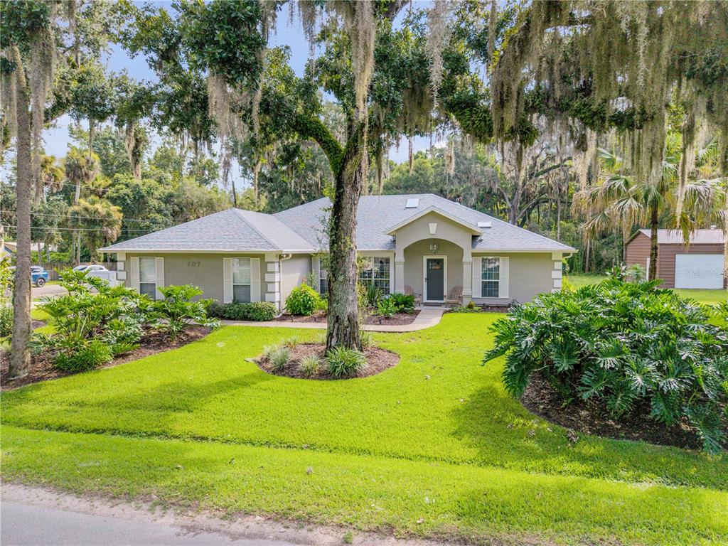 A single-story house with a gray roof, tan exterior, and large trees in the yard — 707 CORBIN PARK ROAD, NEW SMYRNA BEACH, FL