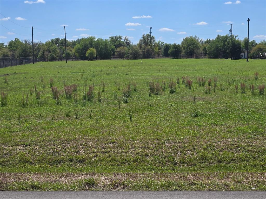 A large, flat, grassy vacant lot with scattered weeds and utility poles in the background — NW 70 HIGHWAY NW, ARCADIA, FL