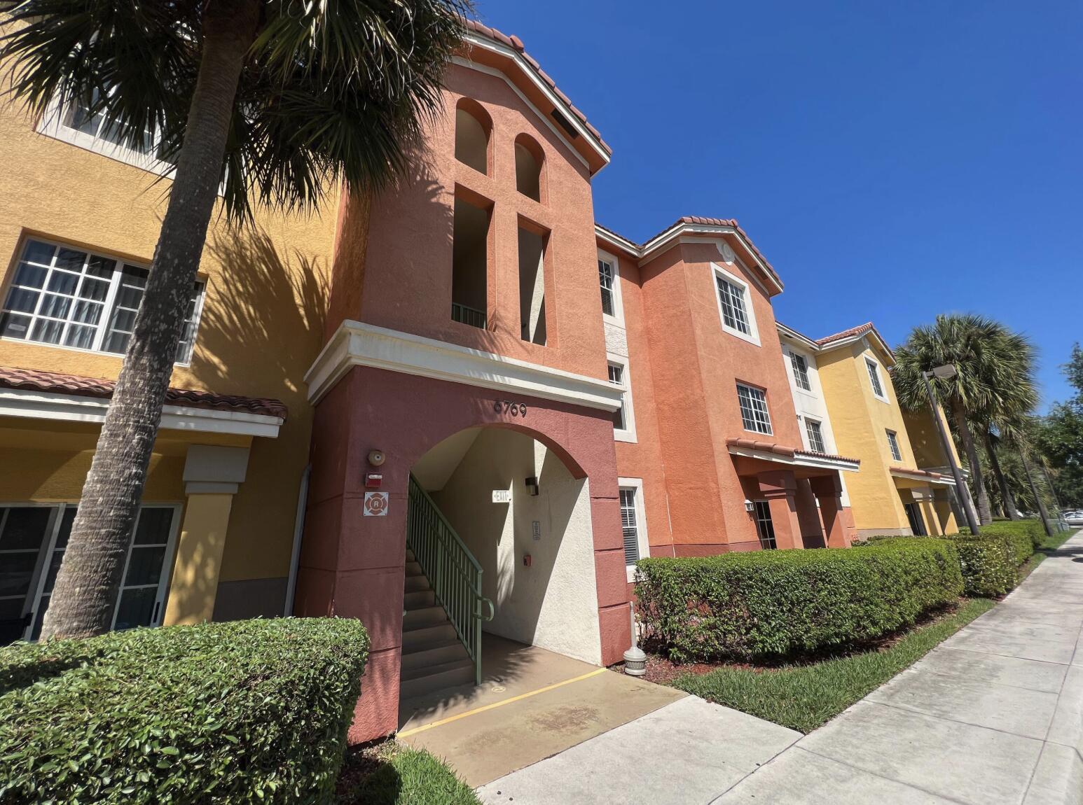 Exterior view of a multi-story apartment building with stucco walls and an arched entryway — 6769 Heritage Grande # 2103, Boynton Beach FL 33437, BOYNTON BEACH, FL