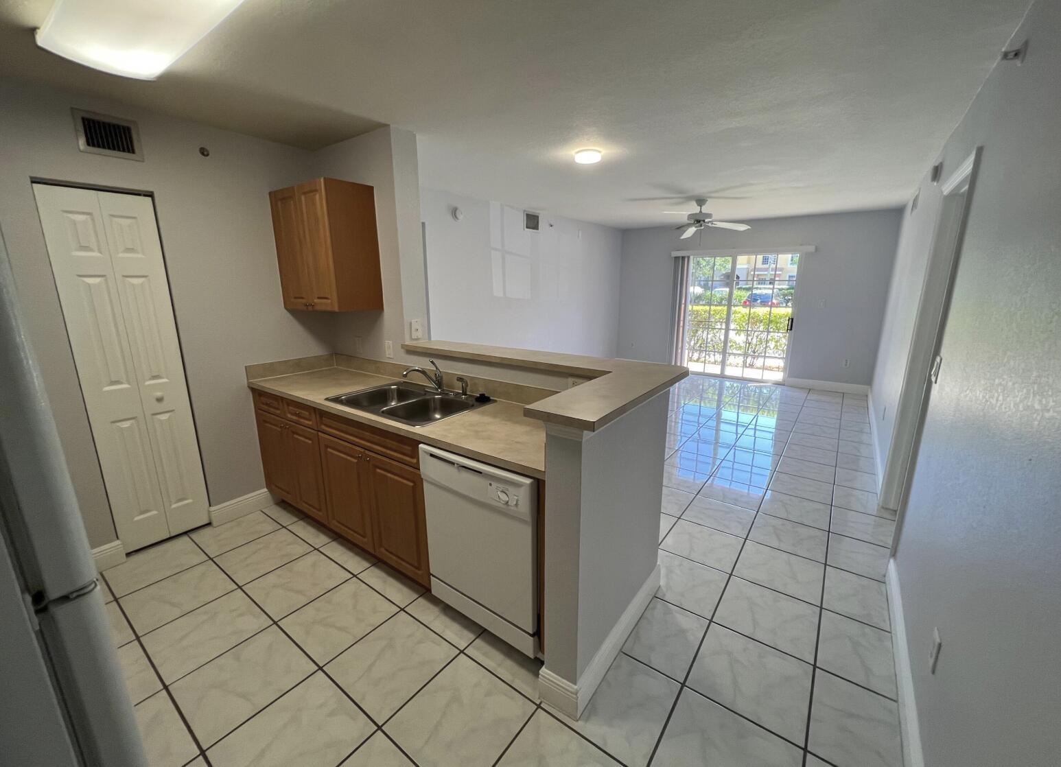A kitchen with wood cabinets and a dishwasher opens to a tiled living area — 6769 Heritage Grande # 2103, Boynton Beach FL 33437, BOYNTON BEACH, FL