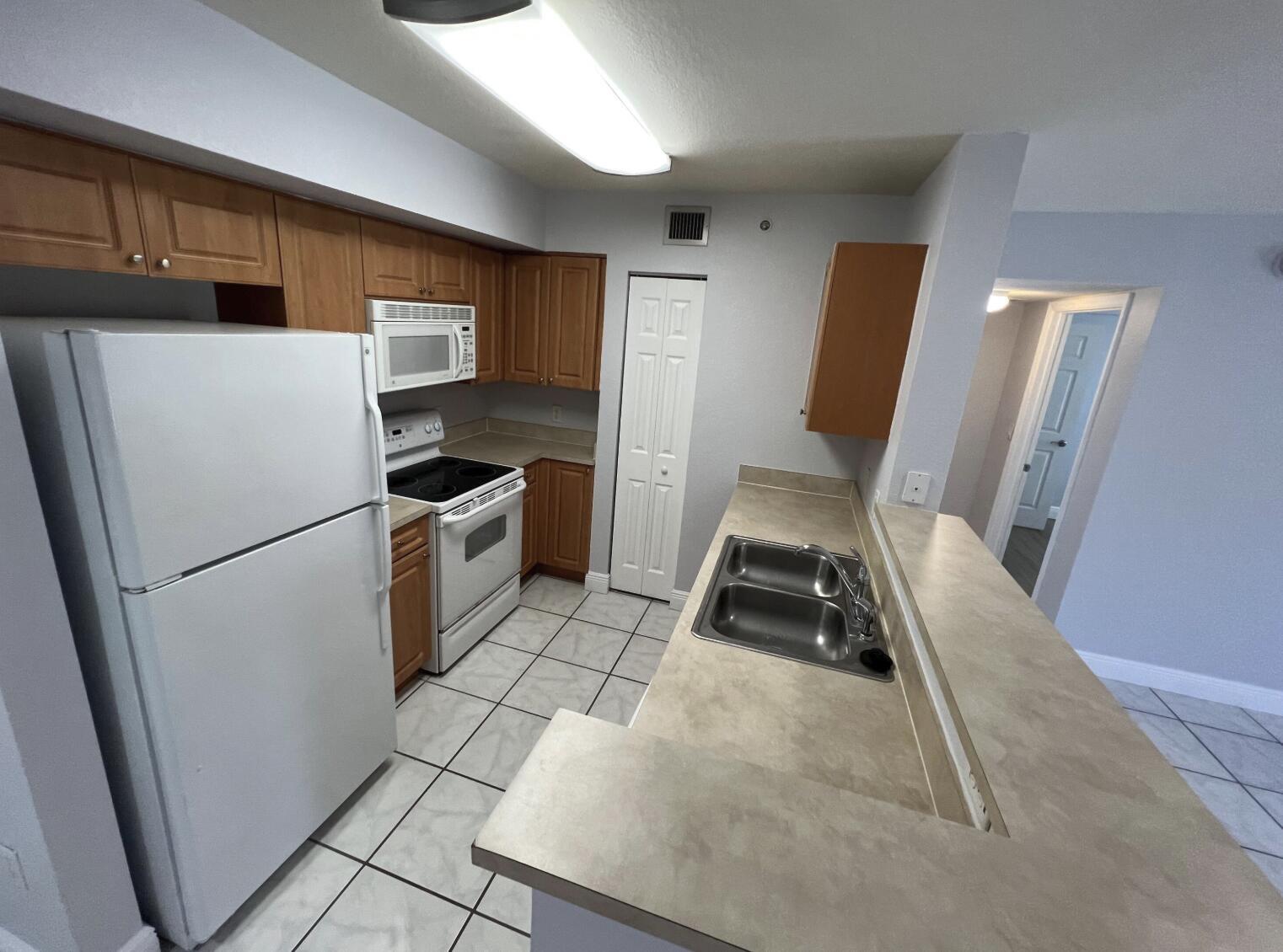 A kitchen features wood cabinets, white appliances, a double sink, and light-colored tile flooring — 6769 Heritage Grande # 2103, Boynton Beach FL 33437, BOYNTON BEACH, FL