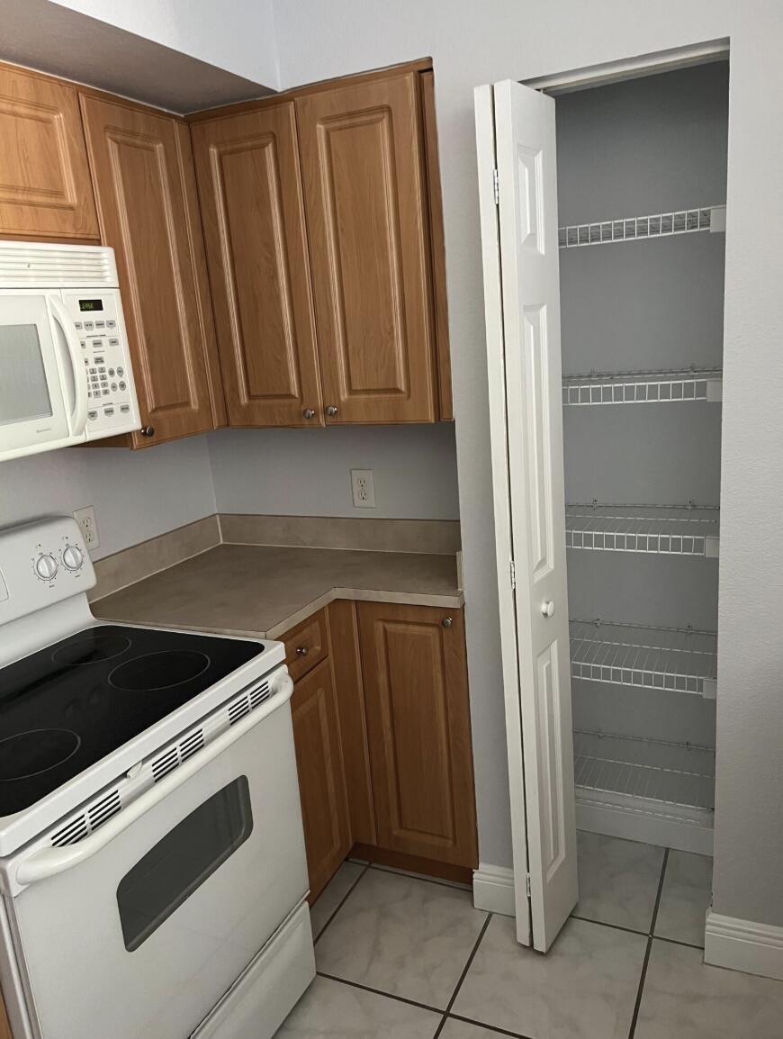 A kitchen features wood cabinets, a white stove, a microwave, and an open pantry closet — 6769 Heritage Grande # 2103, Boynton Beach FL 33437, BOYNTON BEACH, FL