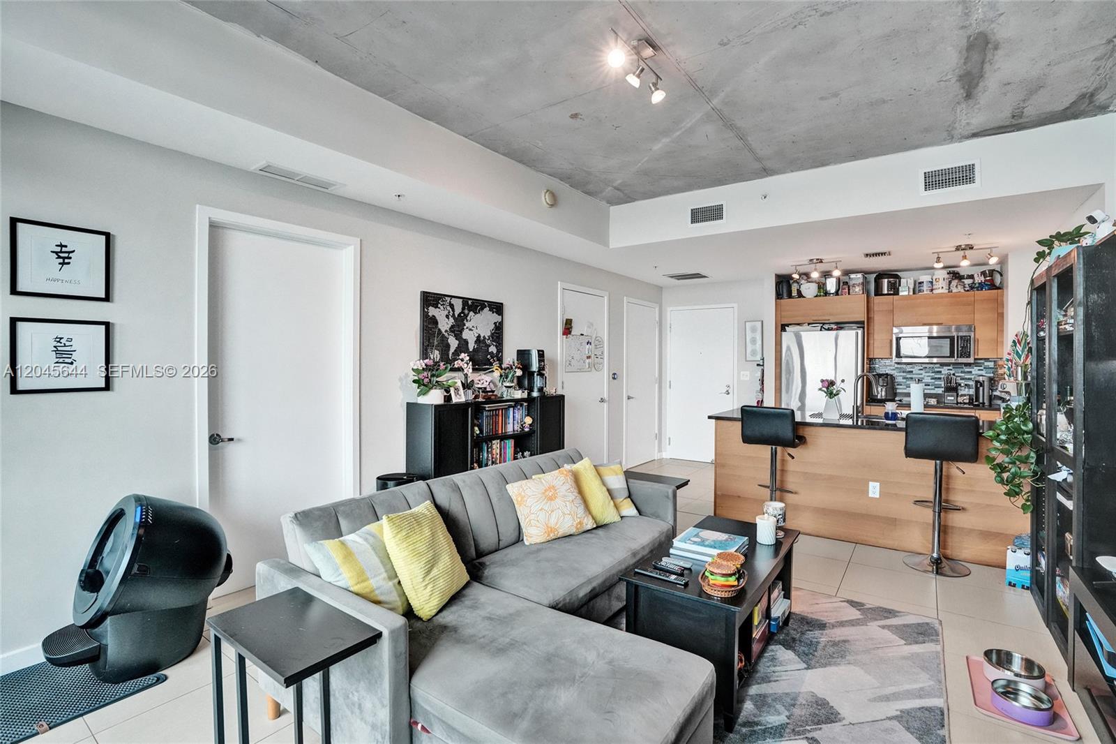 A living room with a gray sectional sofa, open kitchen, and exposed concrete ceiling — 3301 NE 1st Ave # H2405, Miami FL 33137, MIAMI, FL
