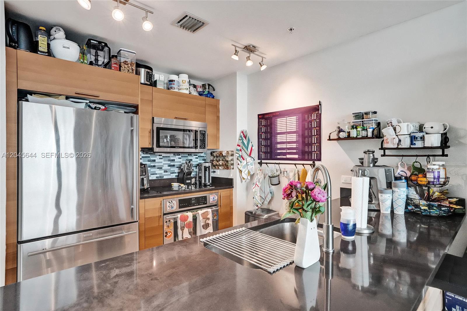 A modern kitchen features stainless steel appliances, wood cabinetry, and a dark stone island countertop — 3301 NE 1st Ave # H2405, Miami FL 33137, MIAMI, FL