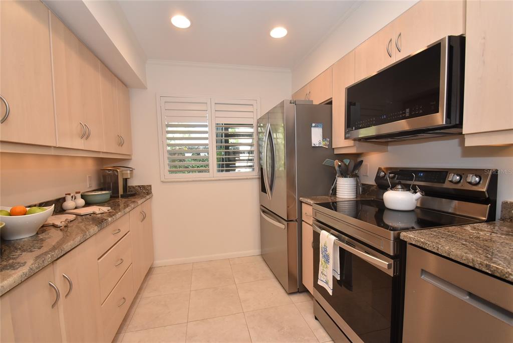 A galley kitchen features light wood cabinets, stainless steel appliances, and granite countertops — 1510 PELICAN POINT DR UNIT BA168, SARASOTA, FL