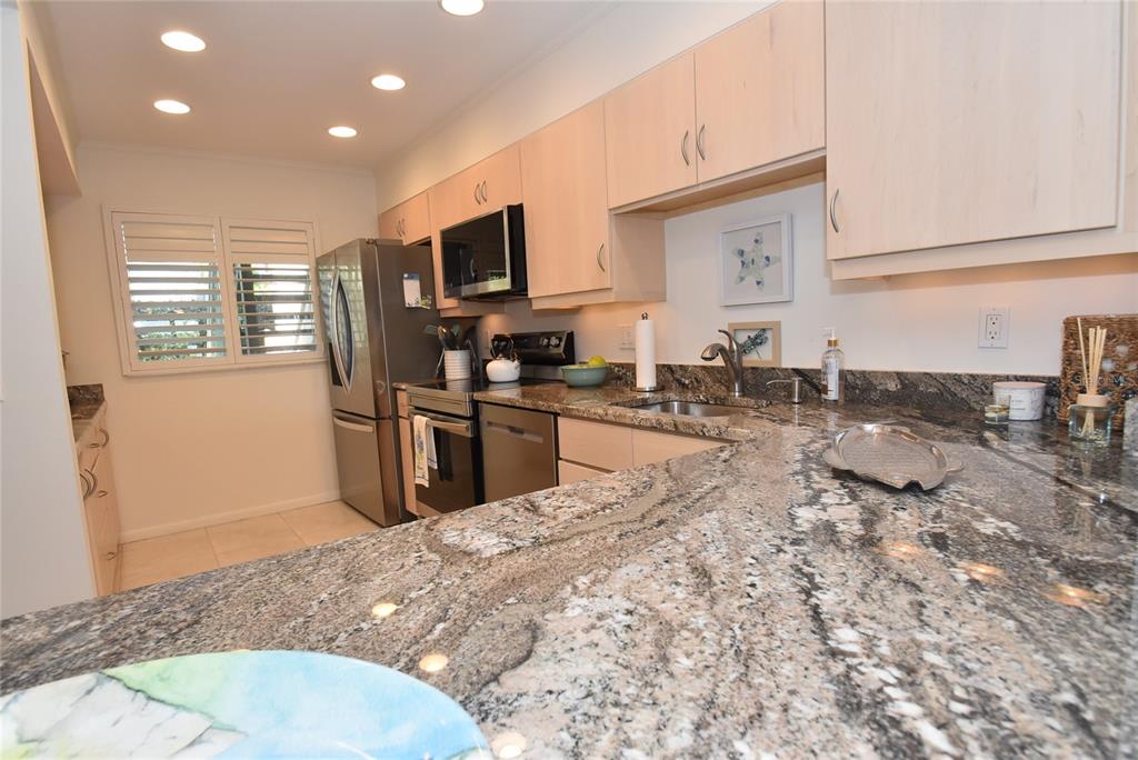 A kitchen features light wood cabinets, granite countertops, and stainless steel appliances — 1510 PELICAN POINT DR UNIT BA168, SARASOTA, FL