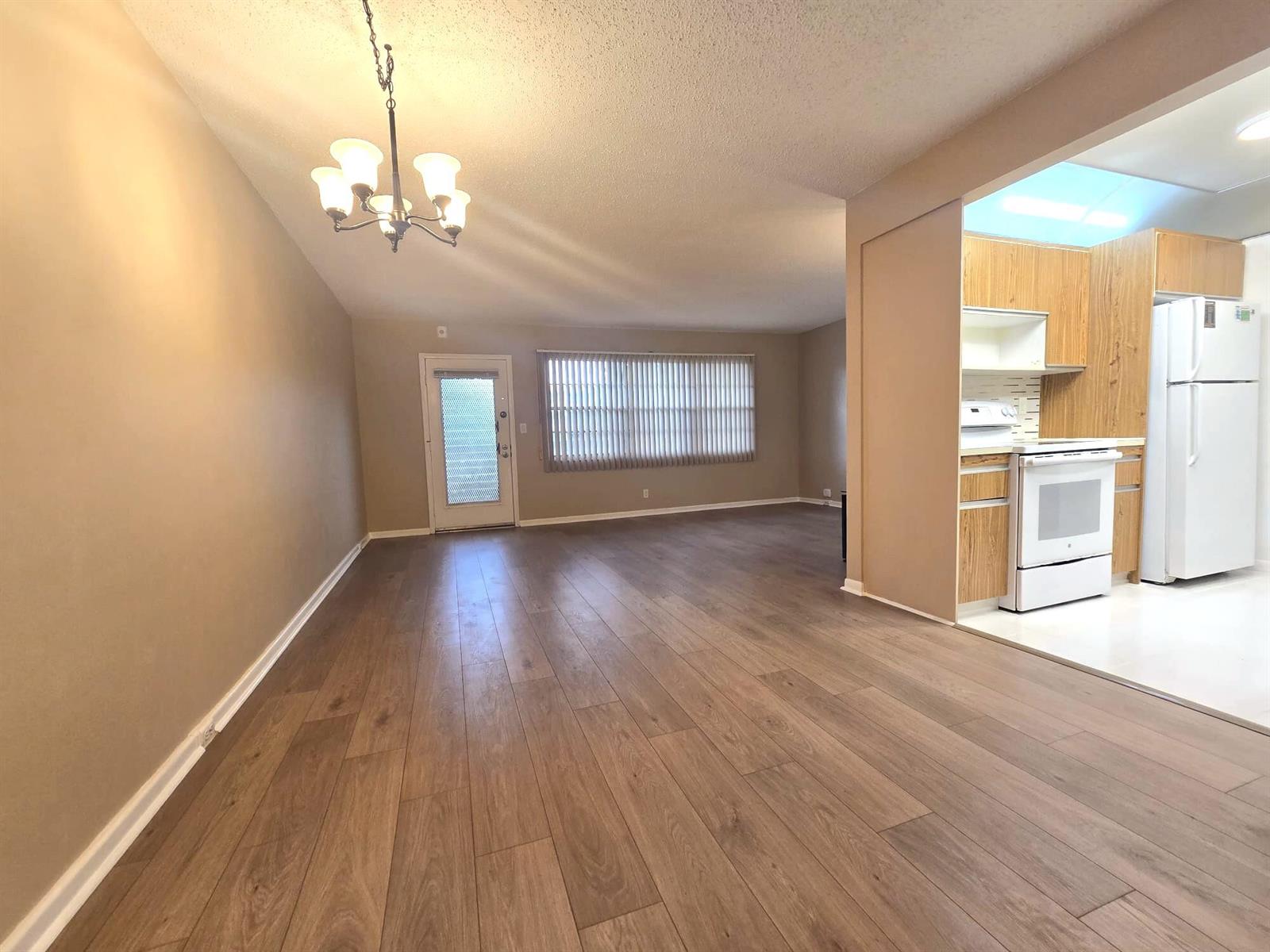 An open-concept living area with wood-look flooring leads into a kitchen with light wood cabinets — 2103 Lucaya Bend # E2, Coconut Creek FL 33066, COCONUT CREEK, FL