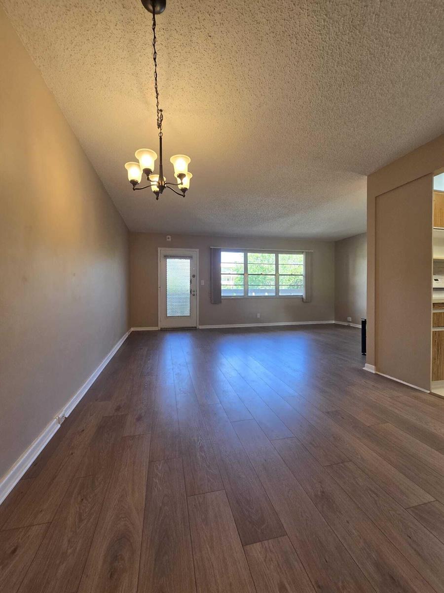 An empty room with wood-look flooring, a chandelier, a glass-paneled door, and a large window — 2103 Lucaya Bend # E2, Coconut Creek FL 33066, COCONUT CREEK, FL
