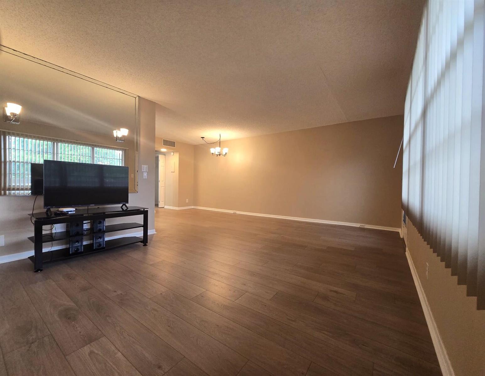 An empty living room features wood-look flooring, a large wall mirror, and a television console — 2103 Lucaya Bend # E2, Coconut Creek FL 33066, COCONUT CREEK, FL
