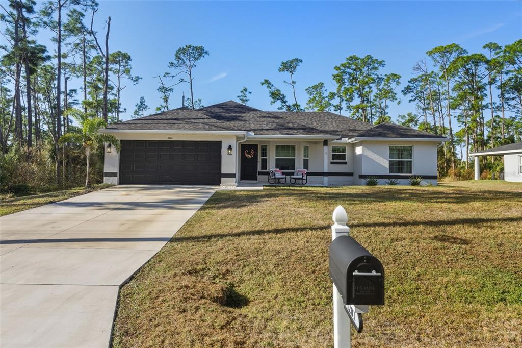 A single-story house with a dark garage door, white stucco exterior, and a front lawn — 1201 LOTUS STREET, PORT CHARLOTTE, FL
