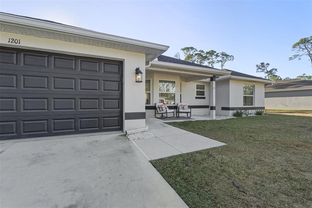 A single-story house exterior features a dark garage door, a covered entryway, and a lawn — 1201 LOTUS STREET, PORT CHARLOTTE, FL