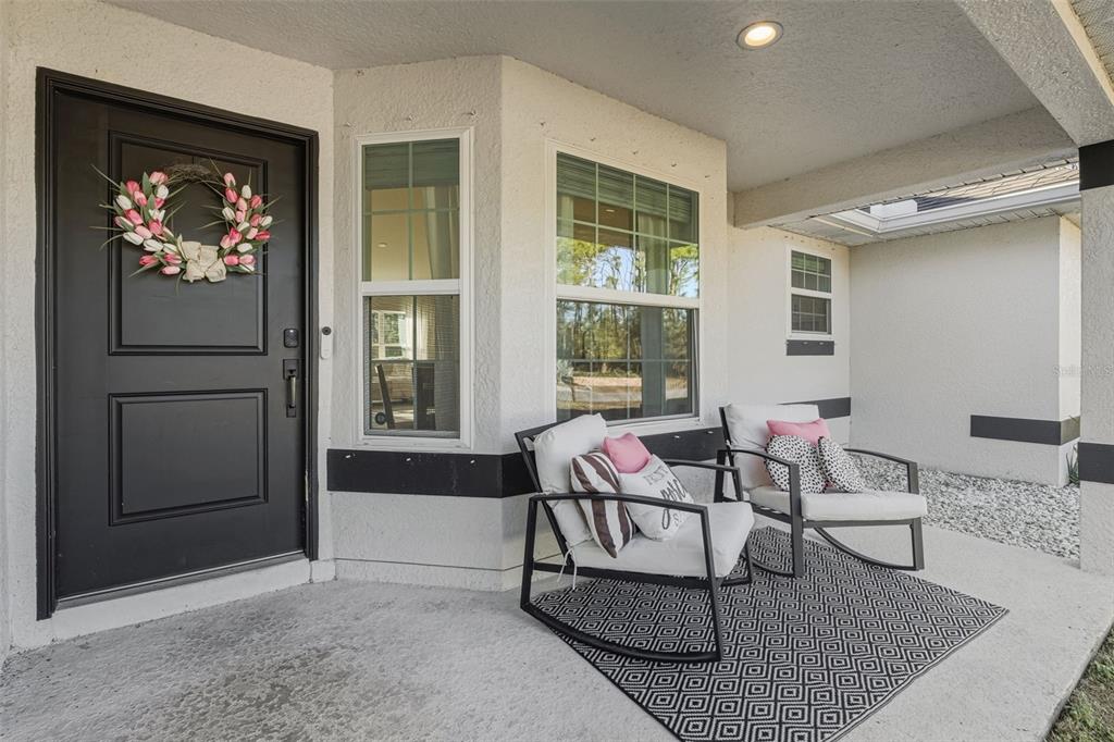 A covered front porch features a black door, two rocking chairs, and a geometric rug — 1201 LOTUS STREET, PORT CHARLOTTE, FL