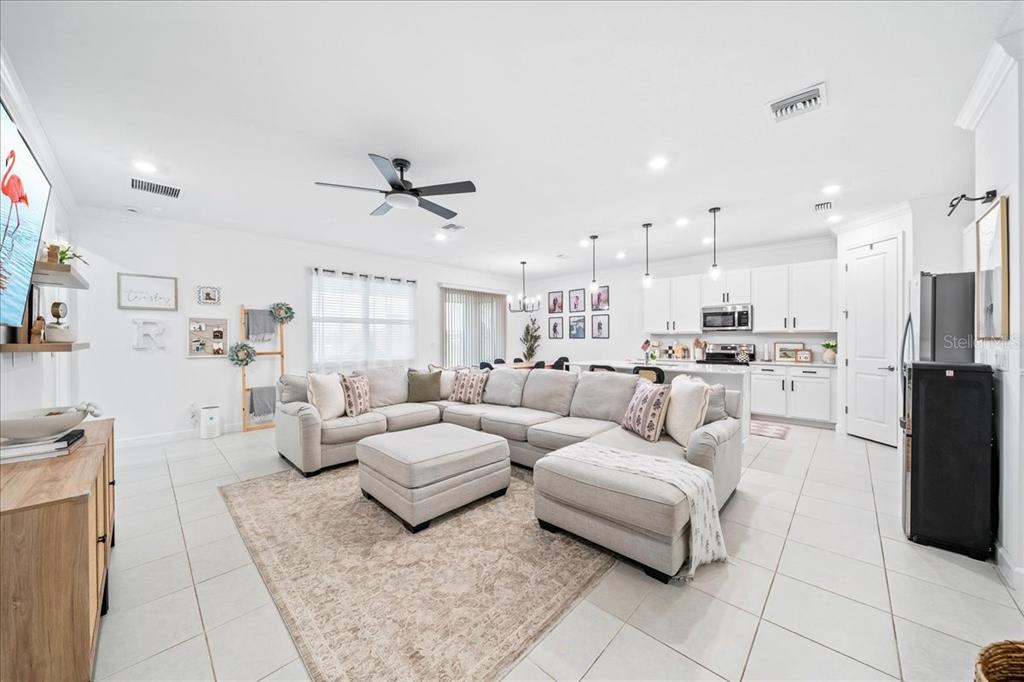 A bright, open-concept living room and kitchen featuring white cabinetry, tile flooring, and a sectional — 732 VERIDIAN CIRCLE NW, PALM BAY, FL