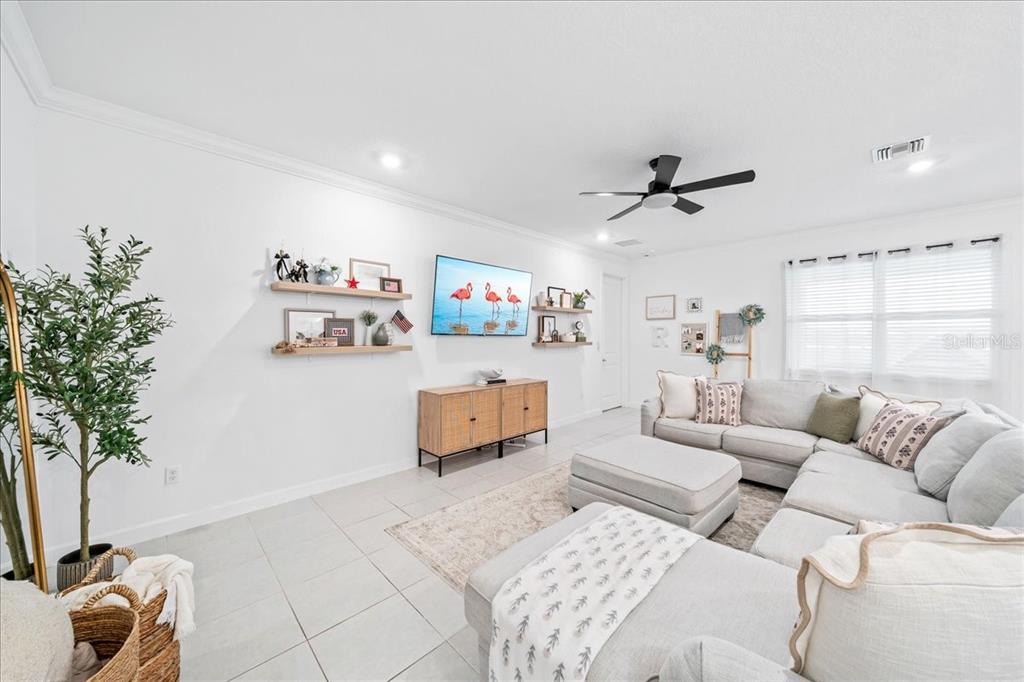 A living room features a light gray sectional sofa, a television, and floating wall shelves — 732 VERIDIAN CIRCLE NW, PALM BAY, FL