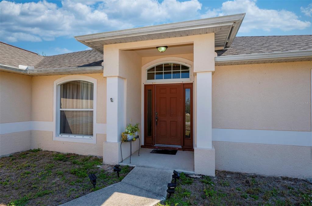 A low-angle view of a house entrance with a brown door, sidelights, and columns — 4129 NE 19TH PLACE, CAPE CORAL, FL