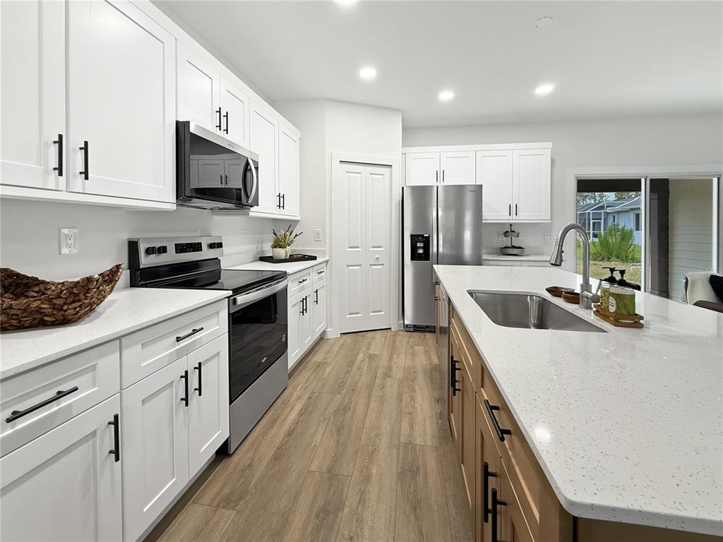 A modern kitchen features white cabinets, a wood-tone island, stainless steel appliances, and quartz countertops — 16419 STRAUSS AVENUE, PORT CHARLOTTE, FL