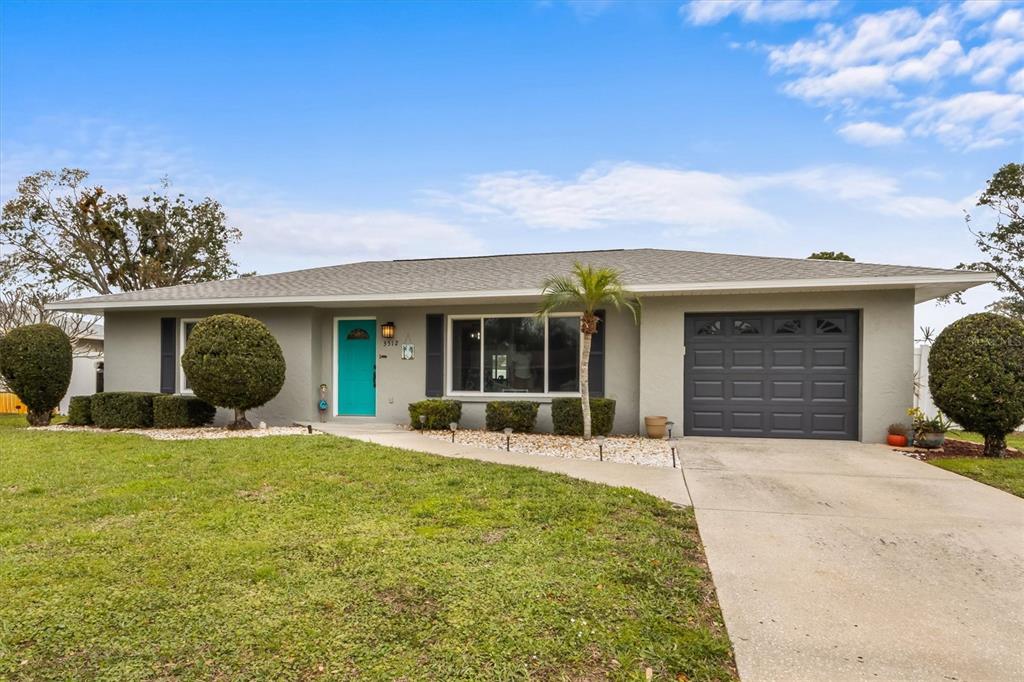 A single-story gray house features a bright teal front door and a one-car garage — 3512 21ST AVENUE W, BRADENTON, FL
