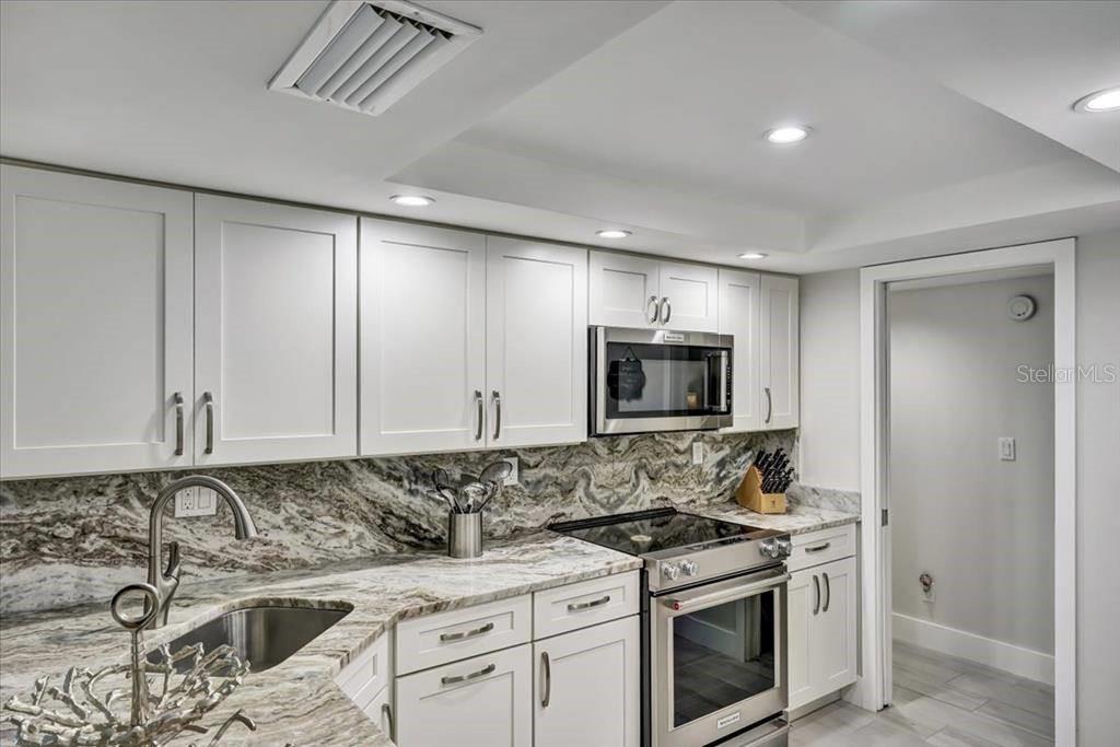 A kitchen features white cabinets, stainless steel appliances, and a patterned stone countertop and backsplash — 6046 W PEPPERTREE WAY UNIT 223B, SARASOTA, FL