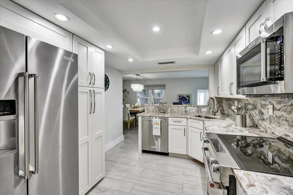 A modern kitchen features white cabinetry, stainless steel appliances, and granite countertops — 6046 W PEPPERTREE WAY UNIT 223B, SARASOTA, FL