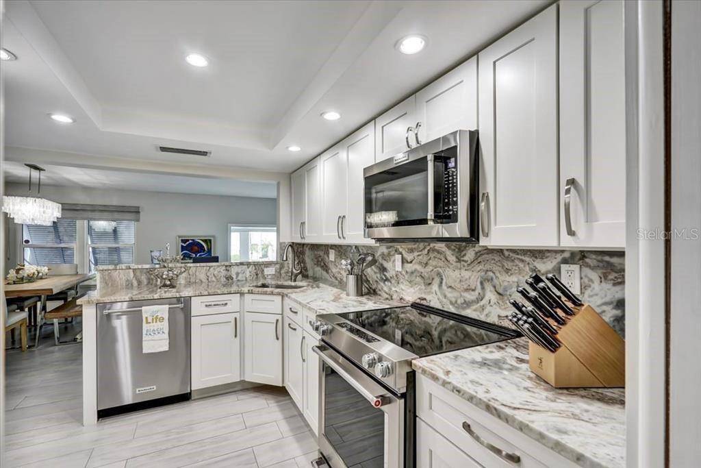 A modern kitchen features white cabinets, marble countertops, stainless steel appliances, and tile flooring — 6046 W PEPPERTREE WAY UNIT 223B, SARASOTA, FL