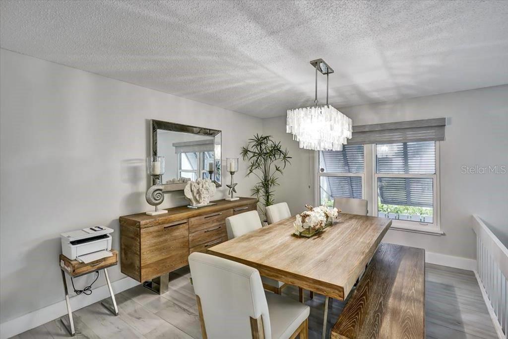 A dining room features a wooden table, bench seating, white chairs, and a crystal chandelier — 6046 W PEPPERTREE WAY UNIT 223B, SARASOTA, FL