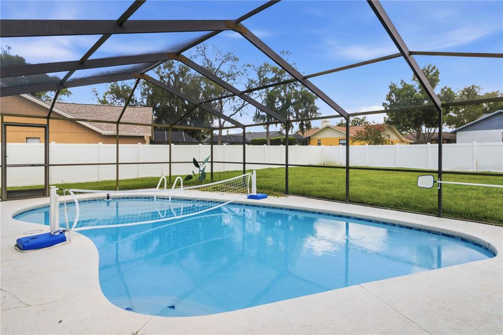 A swimming pool with a volleyball net sits inside a screened-in lanai with a backyard — 2110 LAINDALE PLACE, VALRICO, FL